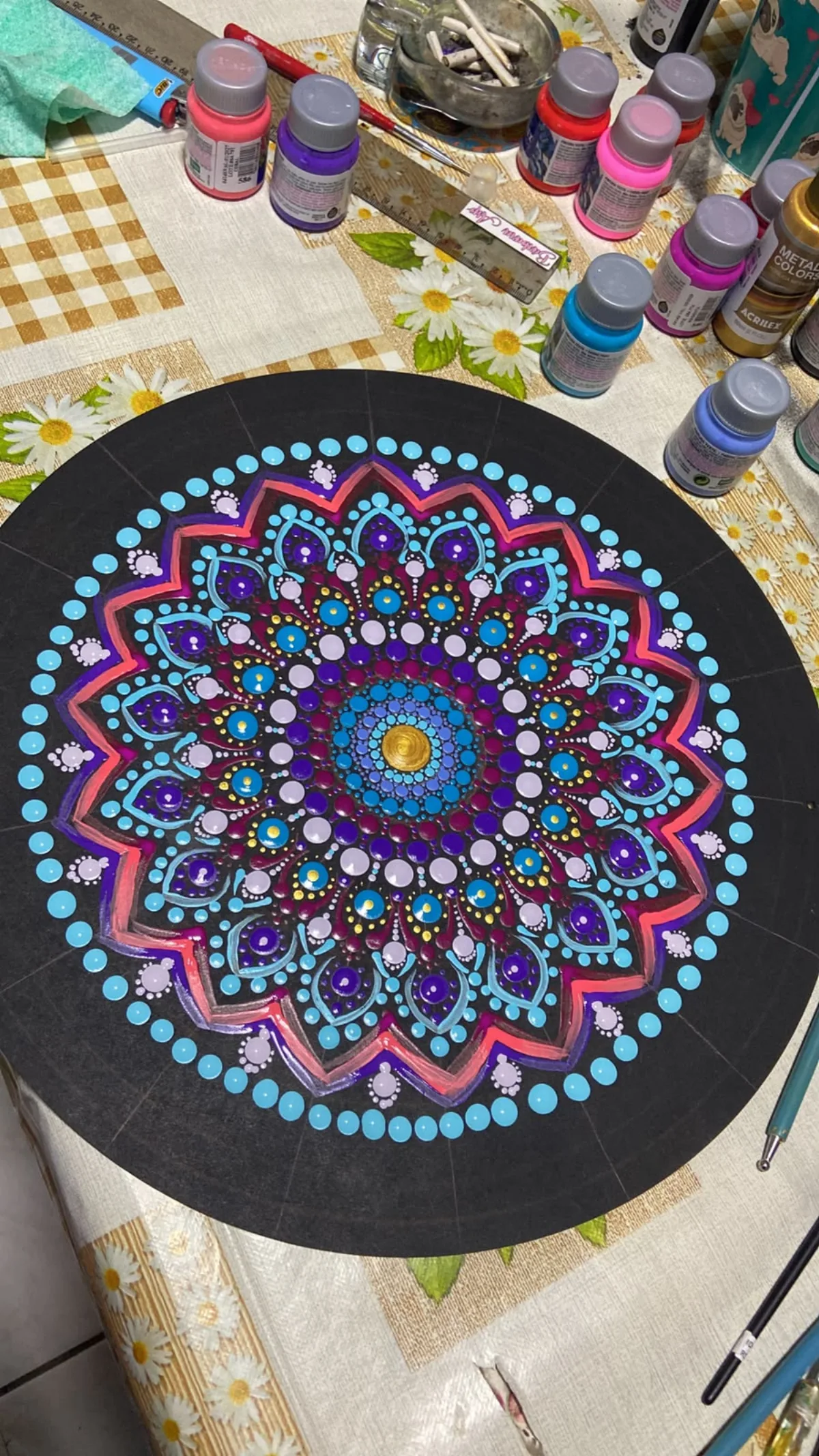 Mandala em processo sobre a mesa do ateliê, cercada de potes de tinta